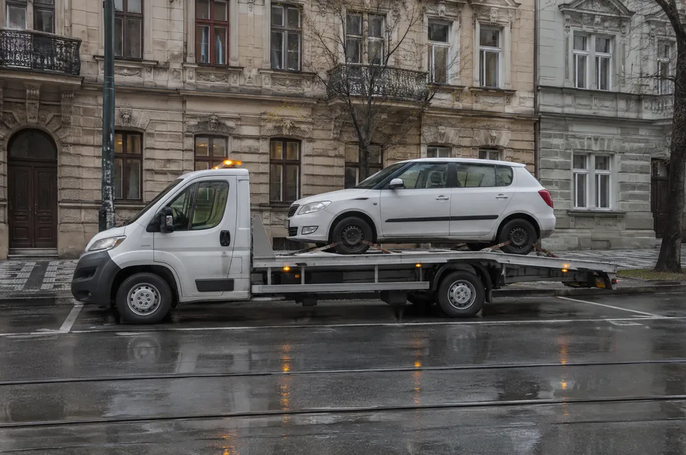 Bílá Škoda Fabia naložená na odtahovce v deštivé Ječné ulici na Novém Městě