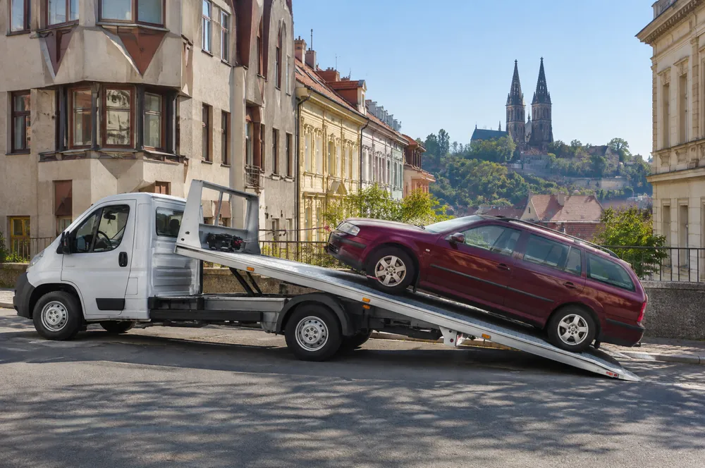 Odtahovka navijákem nakládá vínovou Škodu Octavii combi pod Vyšehradem, nad střechami věže baziliky