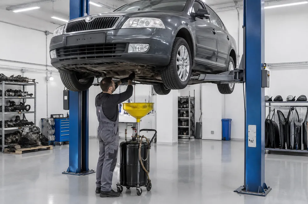 Technik vypouští olej ze spodu převodovky Škody Octavie na zvedáku do sběrné nádoby